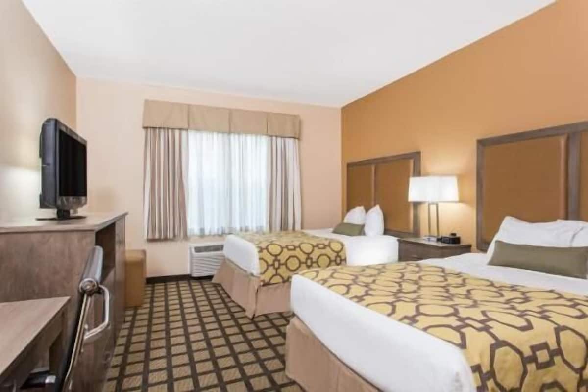 Ein Hotelzimmer mit zwei Betten, einem Fernseher, einem Schreibtisch und einem Fenster mit Vorhängen.