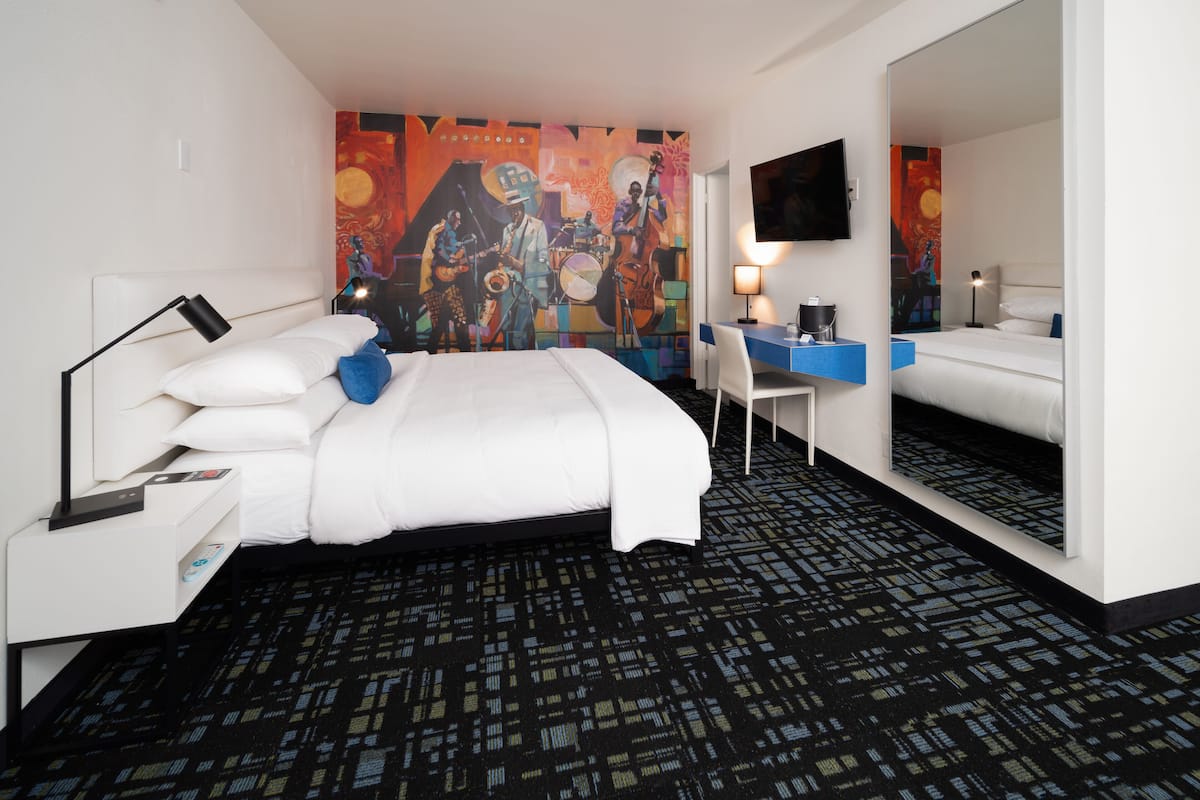 A hotel room with a bed, desk, chair, and a large mirror.