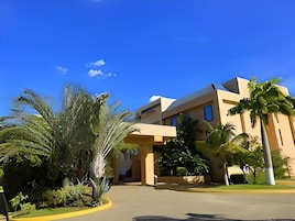 Um edifício moderno com entrada curva, rodeado por palmeiras e vegetação.
