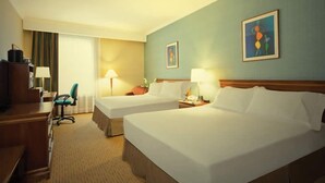 Une chambre d’hôtel avec deux lits, un bureau, une chaise et une lampe.