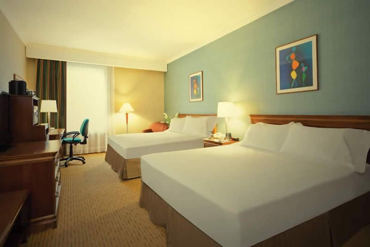 Ein Hotelzimmer mit zwei Betten, einem Schreibtisch, einem Stuhl und einer Lampe.