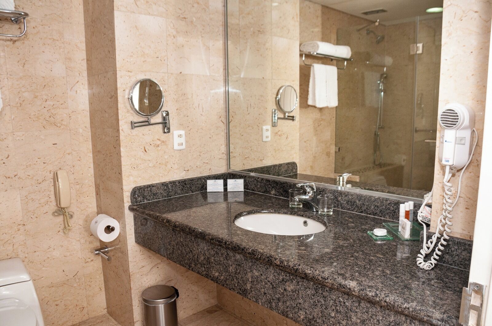 A bathroom with a granite countertop, a white sink, a mirror, a hairdryer, and a towel rack.