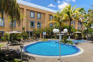 Hotel com piscina, espreguiçadeiras e palmeiras.