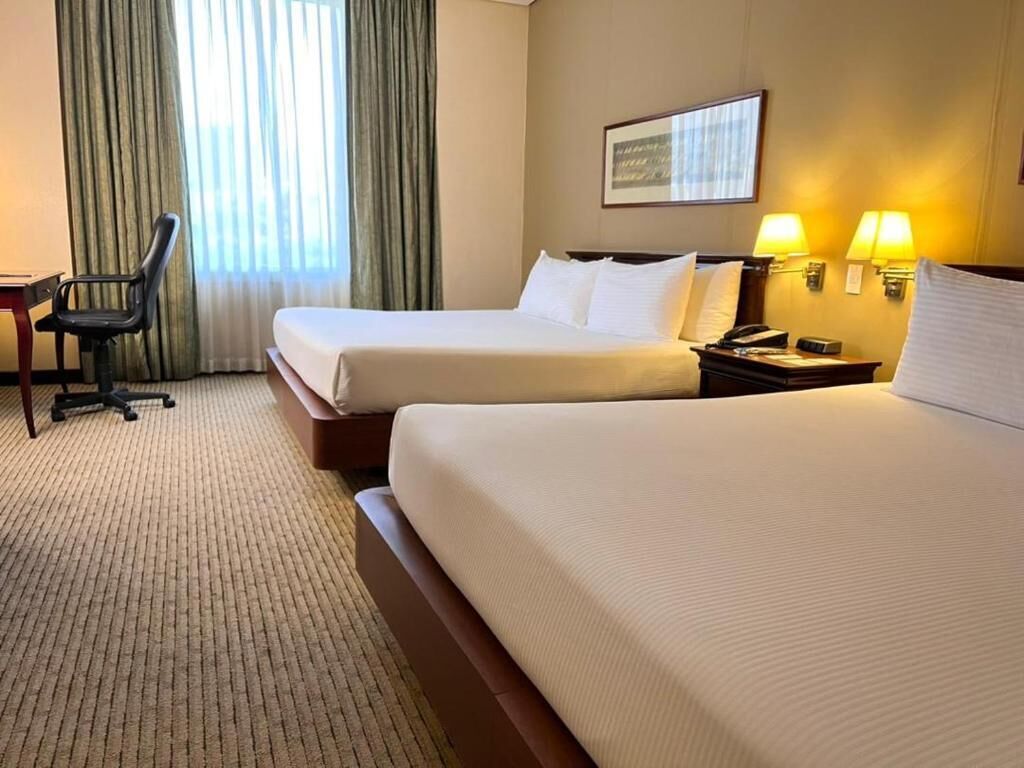 A hotel room with two beds, a desk, a chair, and a window with curtains.