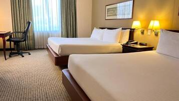 A hotel room with two beds, a desk, a chair, and a window with curtains.