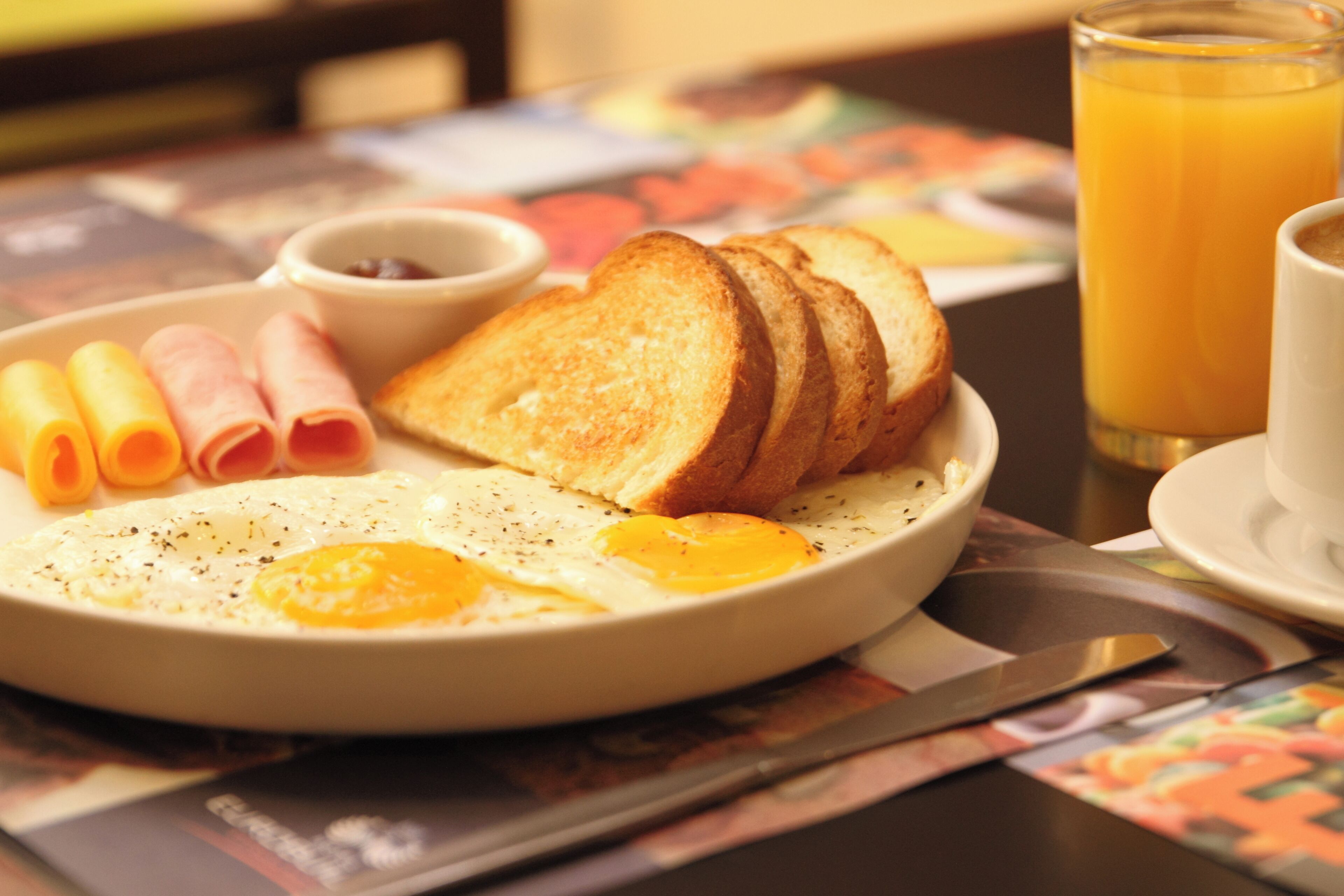 Un plato de desayuno con huevos, jamón, tostadas y un vaso de jugo de naranja.