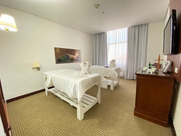 Habitación de hotel con dos camas individuales, un escritorio, una silla, un televisor y un cuadro en la pared.