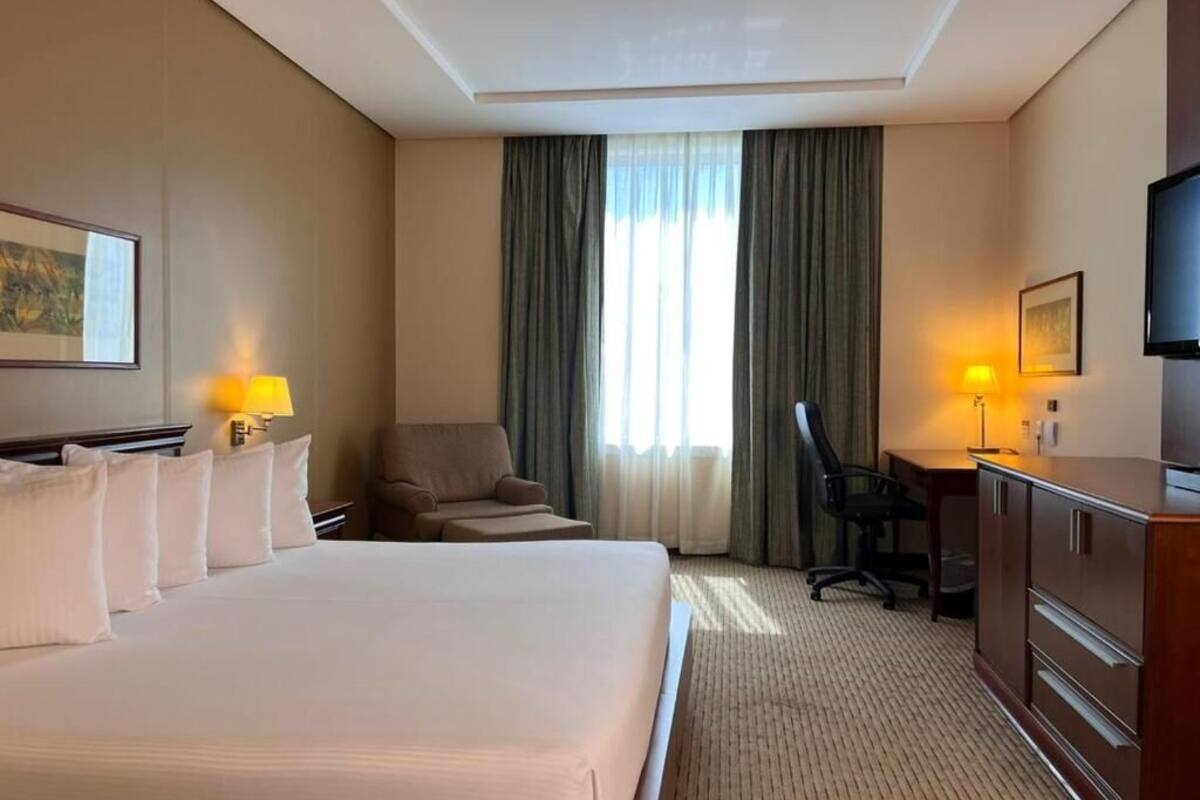 A hotel room with a large bed, a desk, a chair, a television, and a window with curtains.