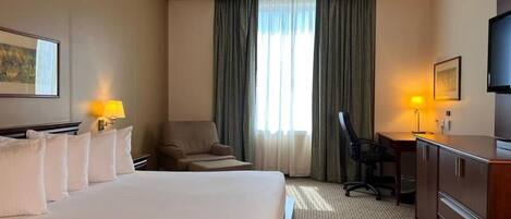 Habitación de hotel con una cama grande, un escritorio, una silla, un televisor y una ventana con cortinas.