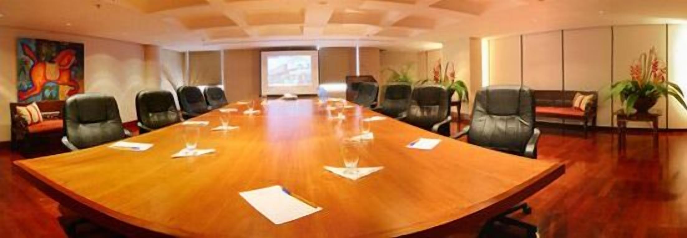 Una sala conferenze con un grande tavolo in legno, diverse sedie, un divano e uno schermo per proiettore.