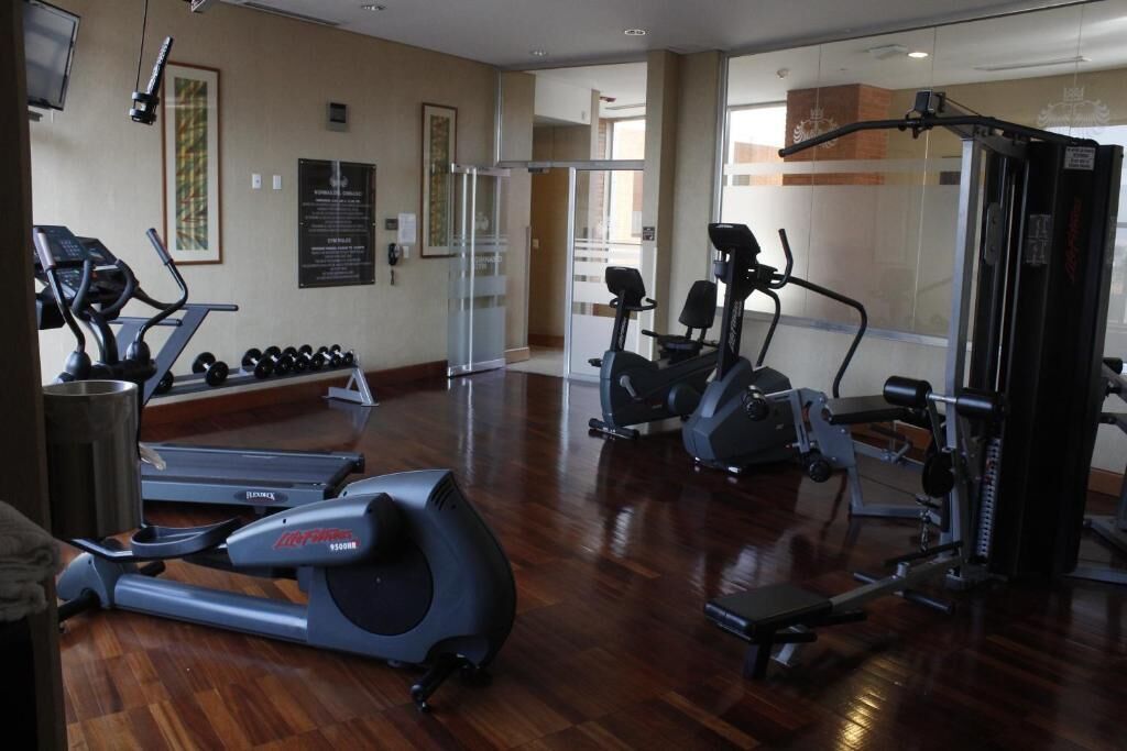 Un gimnasio con cintas de correr, elípticas y equipo de levantamiento de pesas.