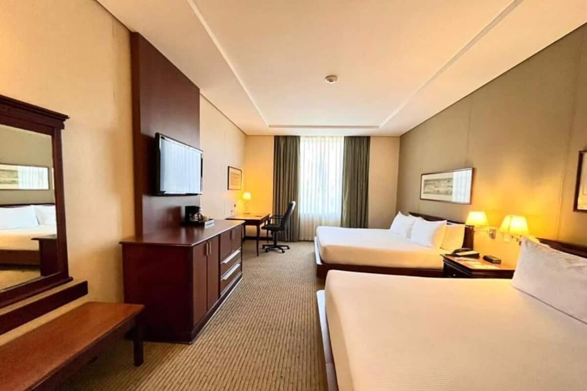 A hotel room with a bed, a desk, a chair, a television, and a window with curtains.