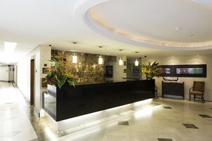 Uma área de recepção moderna com um balcão preto, plantas em vasos e uma parede de destaque em pedra.