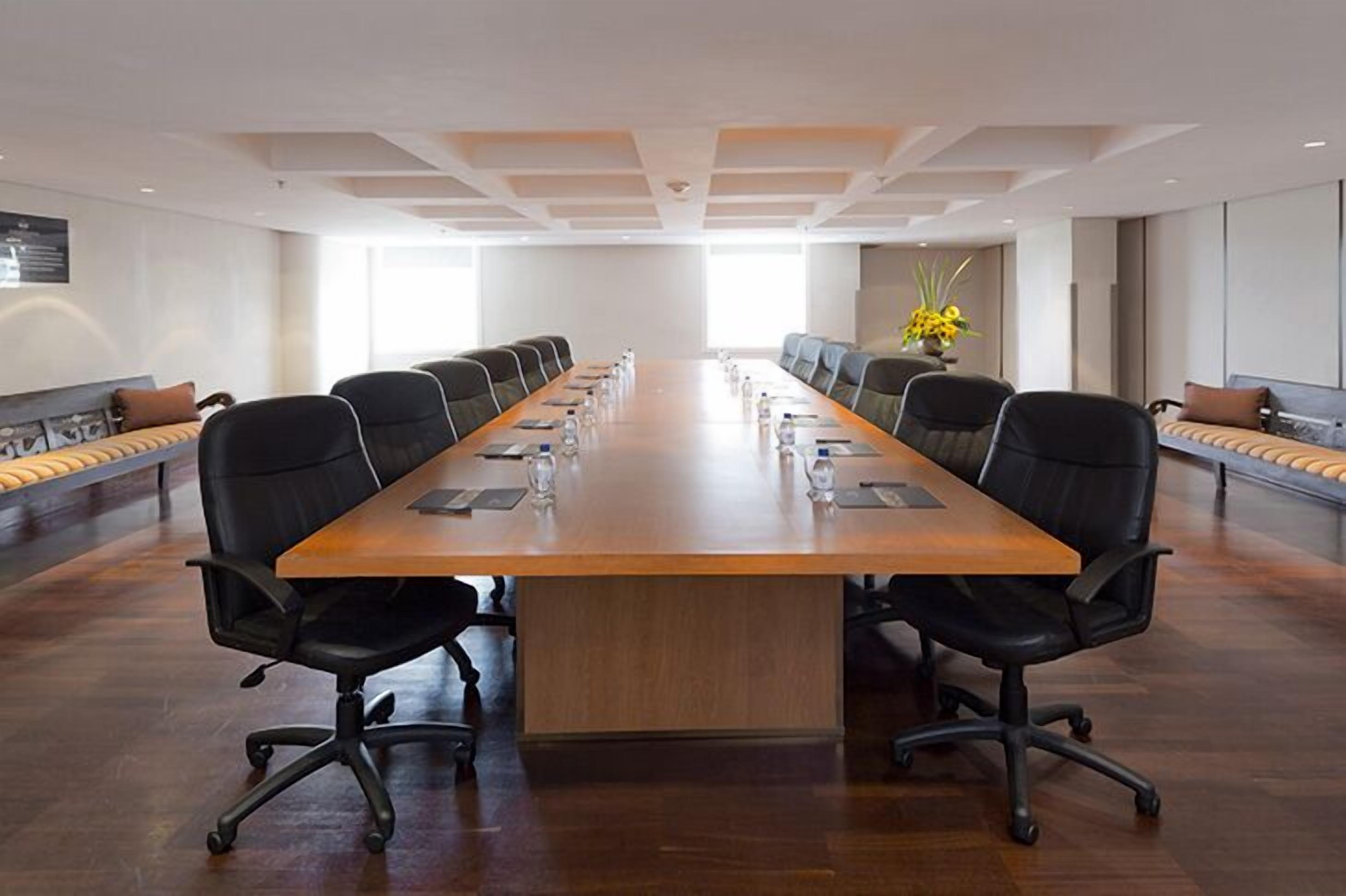 A conference room with a long wooden table, black chairs, and a neutral color scheme.