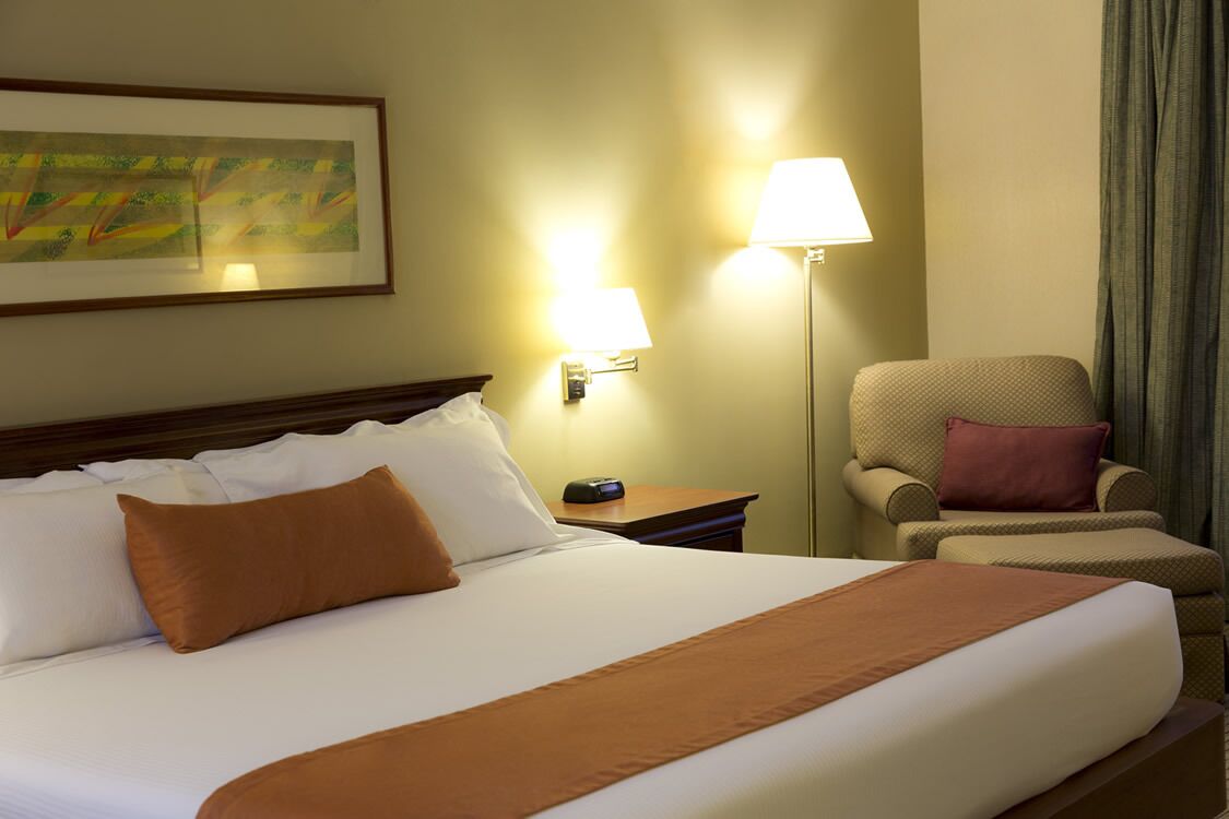 A hotel room with a large bed, two bedside lamps, a chair, and a painting on the wall.
