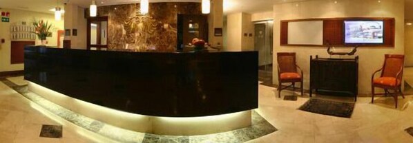 Un área de recepción con un mostrador negro curvo, piso de mármol y dos sillas de madera.