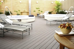 Uma área à beira da piscina com espreguiçadeiras, uma banheira de hidromassagem e um deque de madeira.