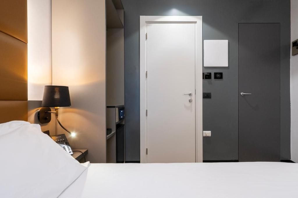 Ein Hotelzimmer mit Bett, Nachttisch mit Lampe, Kleiderschrank und einer Tür mit Bedienfeld.