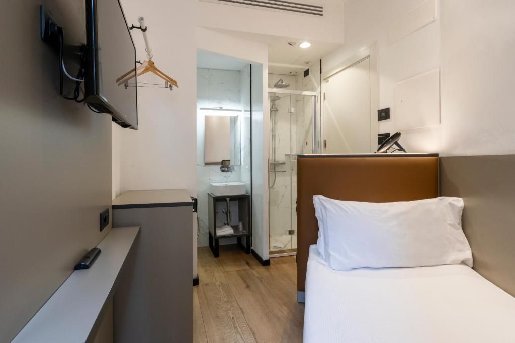 A hotel room with a bed, a desk, a mirror, a shower, and a TV mounted on the wall.