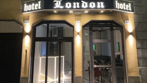 L’entrée d’un hôtel, avec une enseigne indiquant « Hôtel London » et le numéro « 3B » au-dessus de la porte.