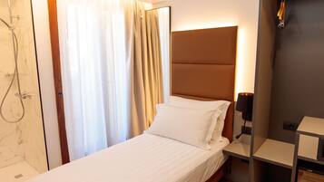 A hotel room with a single bed, a nightstand, a bedside table, a headboard, a shower, and a curtain.