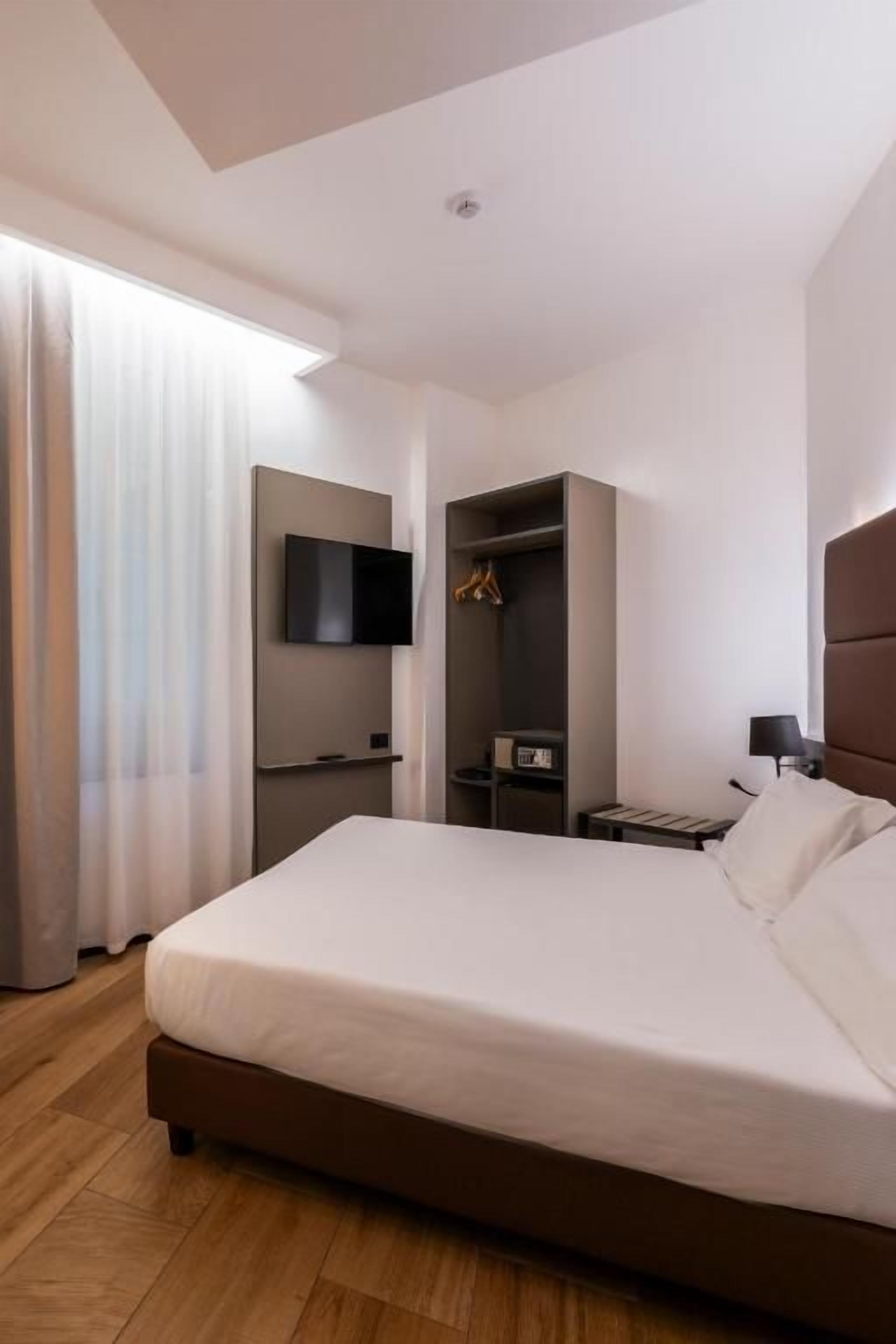 A modern hotel room with a large bed, a flat-screen TV, a wardrobe, and a bedside table.