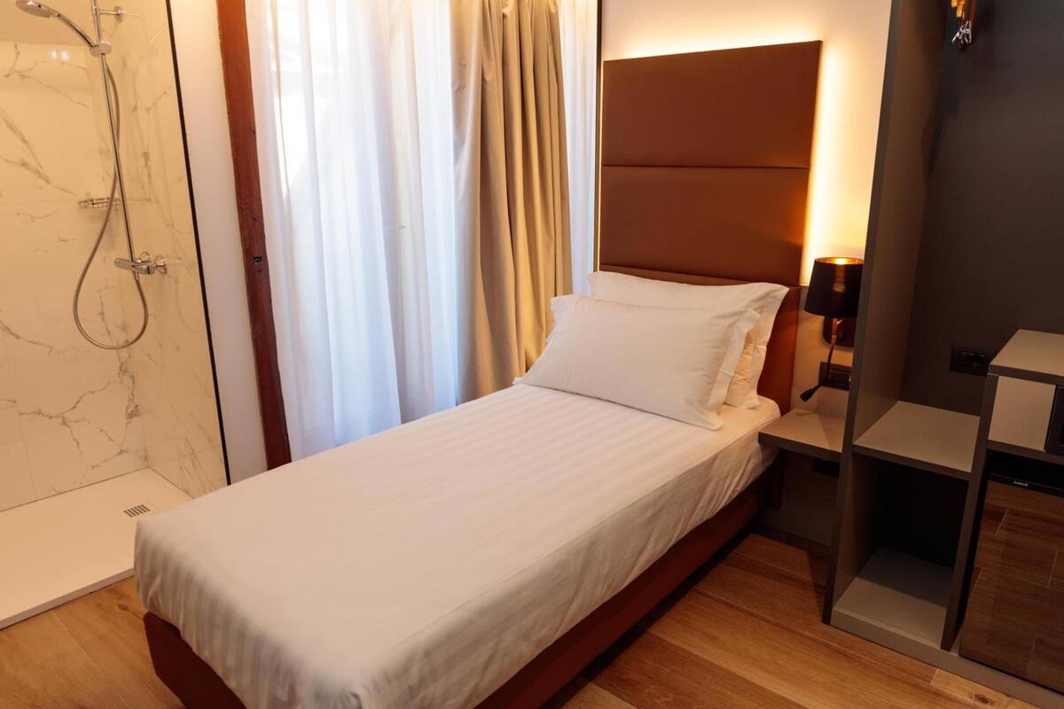 Una camera da letto con un letto, una testiera, un comodino, una lampada e un angolo doccia.