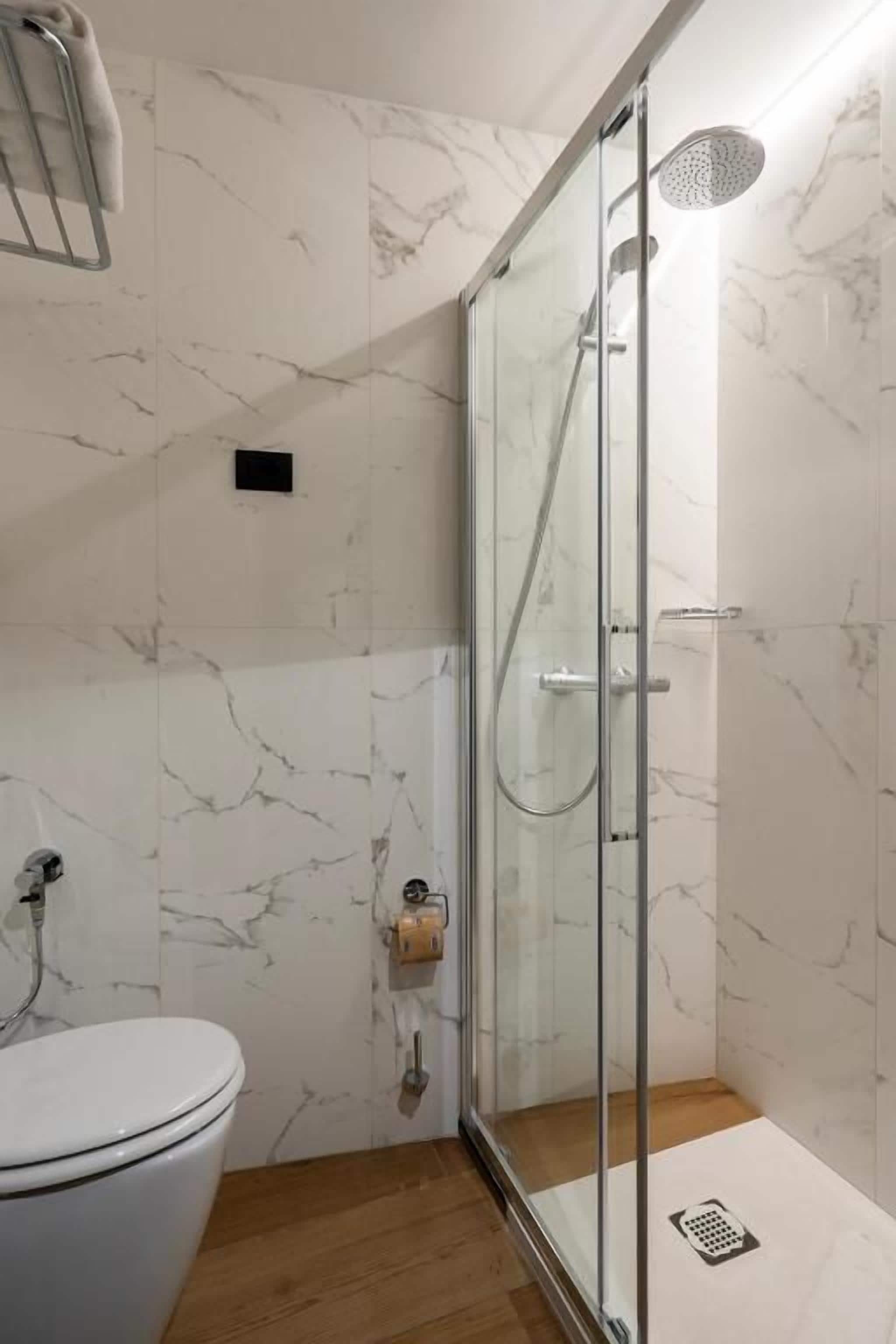 A bathroom with a glass-enclosed shower, a toilet, and marble walls.