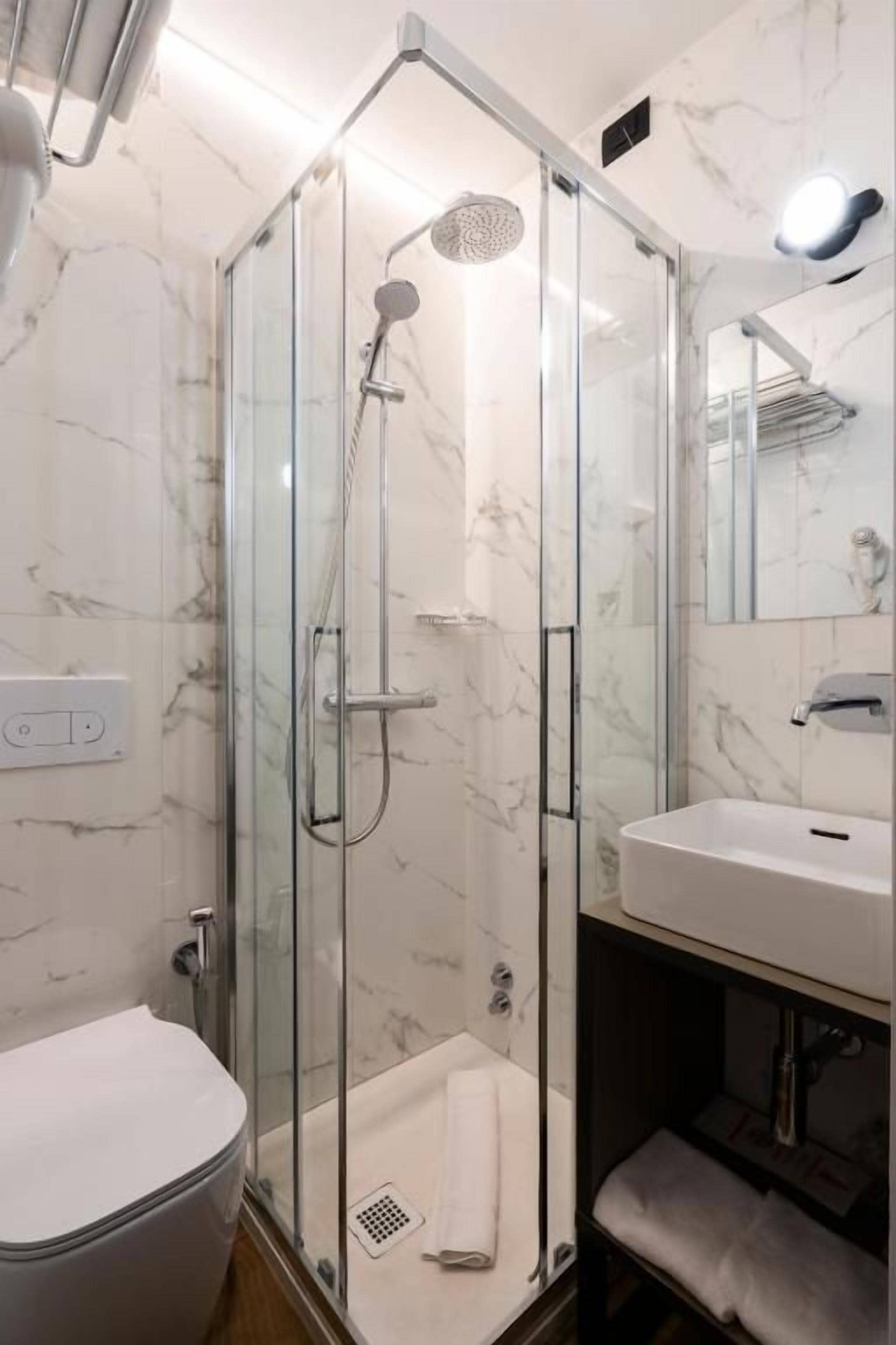 Une salle de bain moderne avec une douche à parois de verre, des toilettes blanches et un lavabo surmonté d’un miroir.