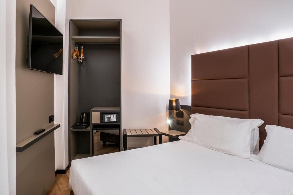 A hotel room with a bed, a bedside table with a lamp, a TV mounted on the wall, and a wardrobe.