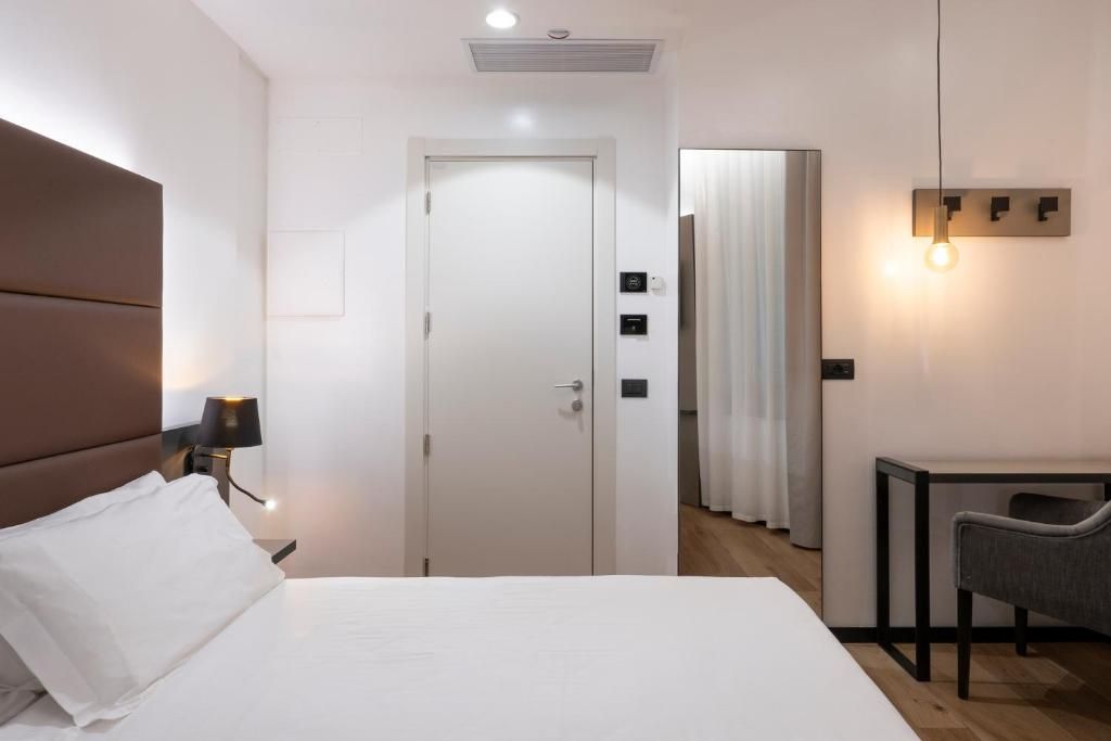 Una habitación de hotel con cama, mesita de noche, lámpara, silla, escritorio y puerta.