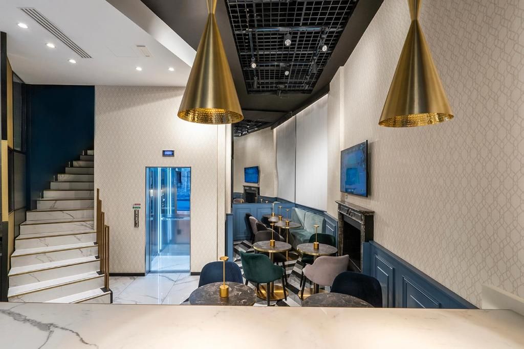 Un intérieur moderne avec un escalier, un espace salon doté de tables rondes et un téléviseur fixé au mur.
