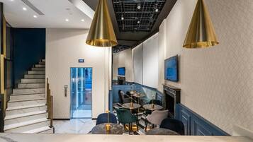 Un intérieur moderne avec un escalier, un espace salon doté de tables rondes et un téléviseur fixé au mur.
