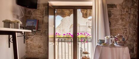 A cozy room with a stone wall, a balcony with flowers, a table with tea set, and a TV on the wall.