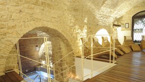 Una habitación con paredes de piedra, suelo de madera, un banco de madera y una barandilla blanca.