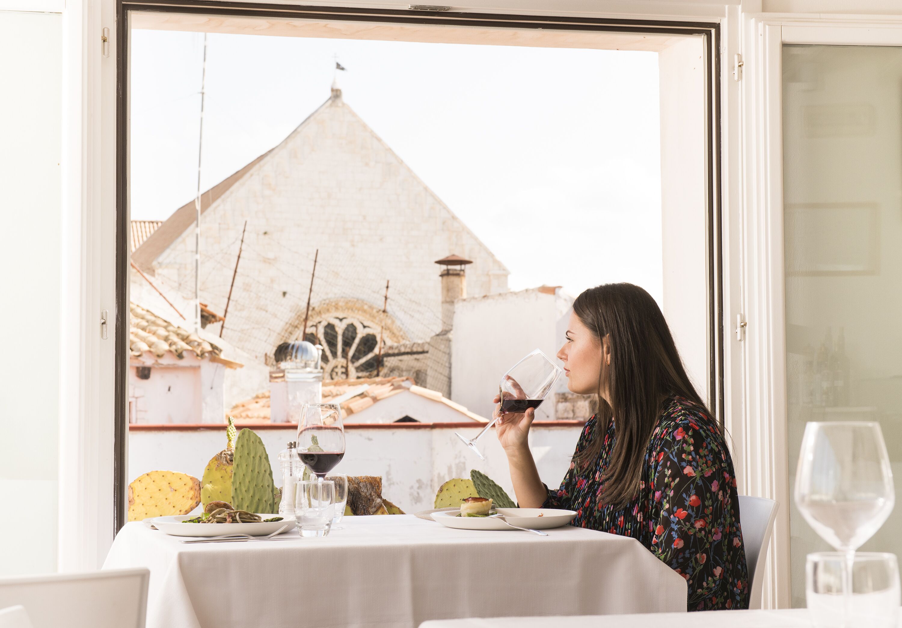 A dining table with a white tablecloth, a glass of red wine, and a plate of food.