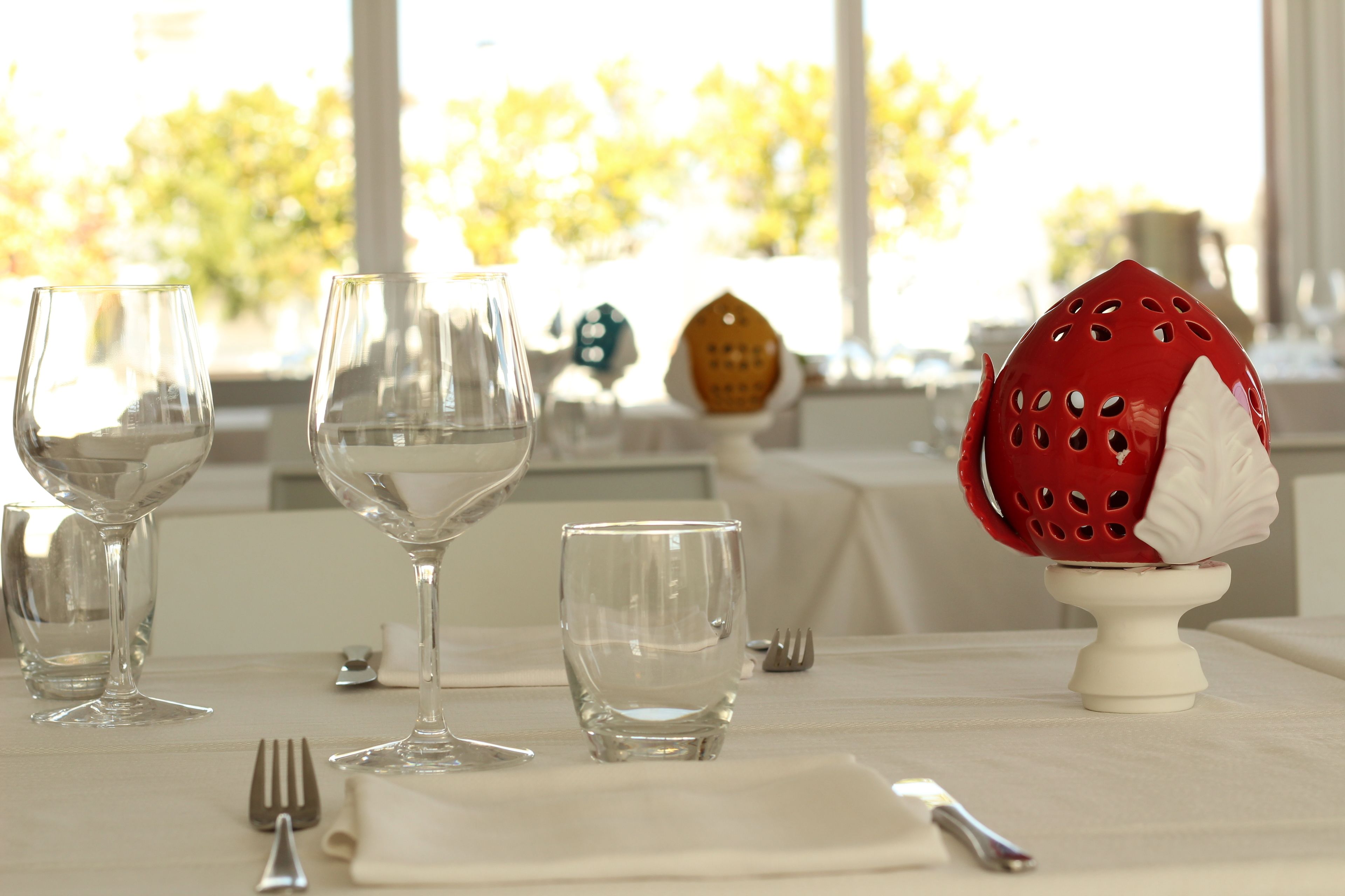 A dining table set with wine glasses, a small glass, a red decorative item, and a white napkin.
