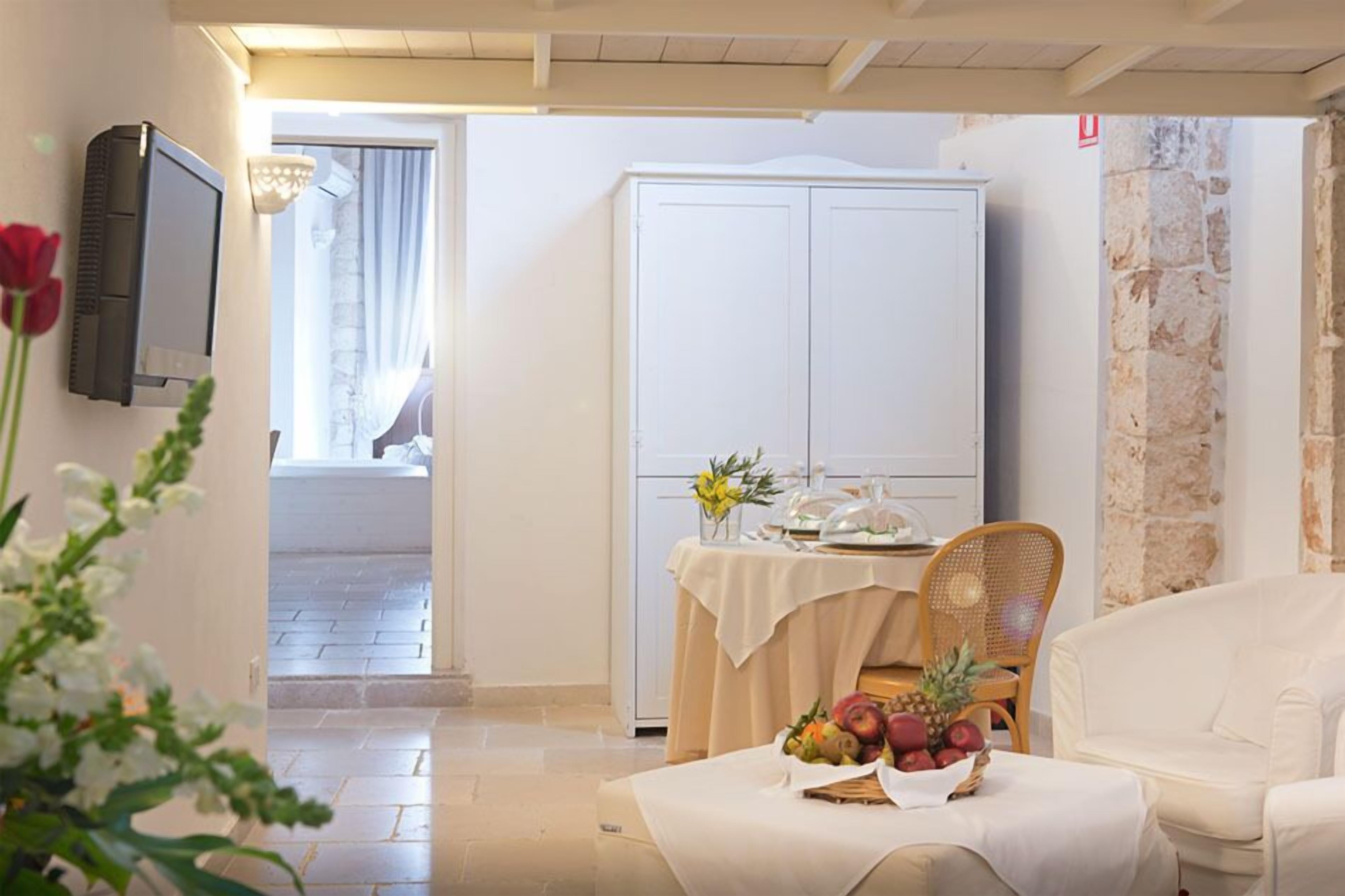 A room with a dining table set for two, a white wardrobe, and a television mounted on the wall.