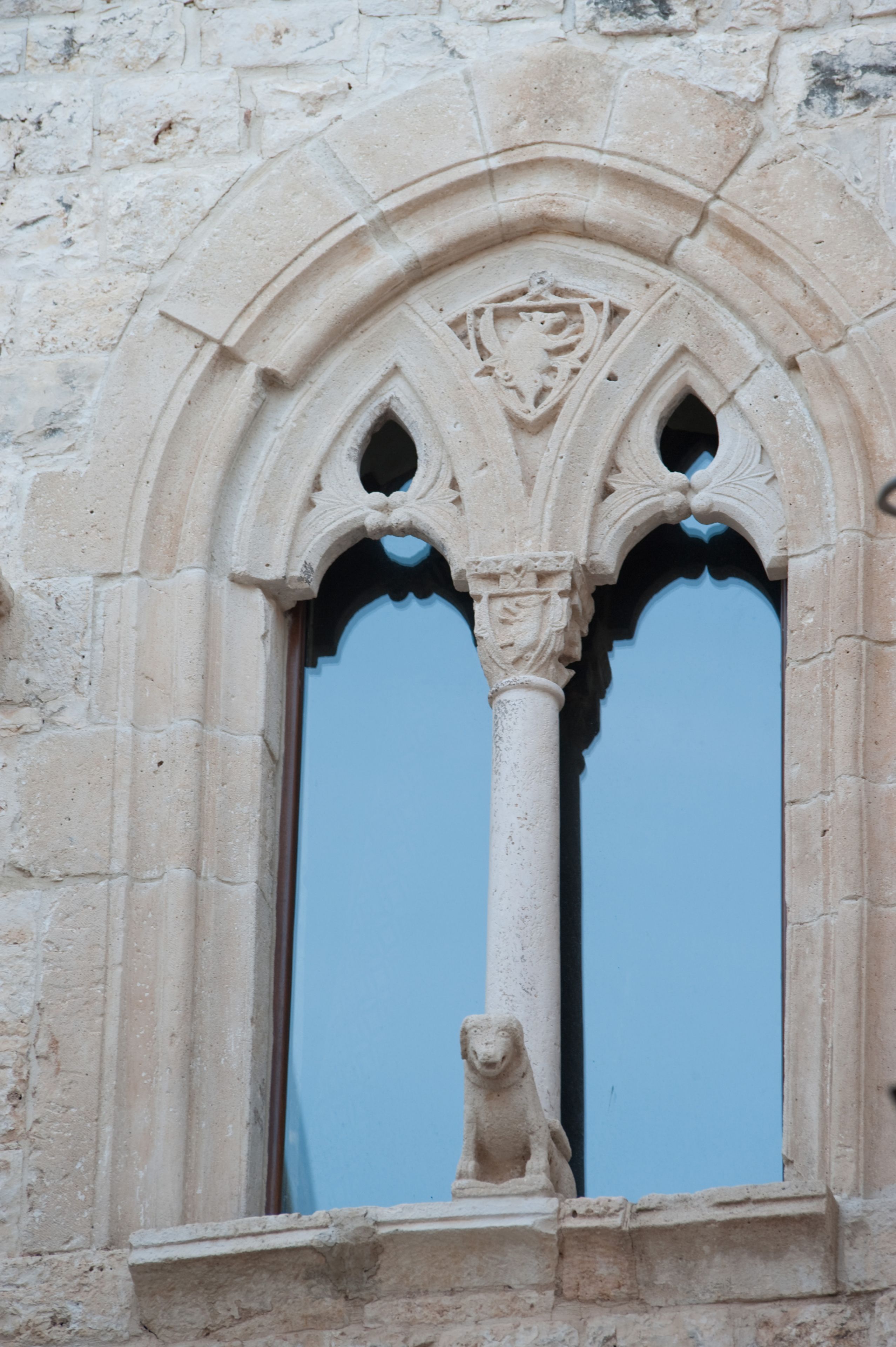 A stone window with a lion statue, Gothic arches, and a blue glass pane.