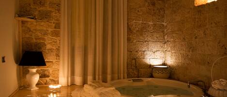 Una habitación con pared de piedra, suelo de madera, bañera y velas.