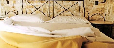 A bed with a metal headboard, white bedding, and a yellow blanket. There are two wall-mounted lamps on either side of the bed.