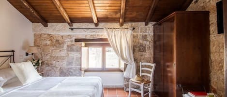 Camera da letto con parete in pietra, travi in legno a vista, un letto, una sedia e un armadio.