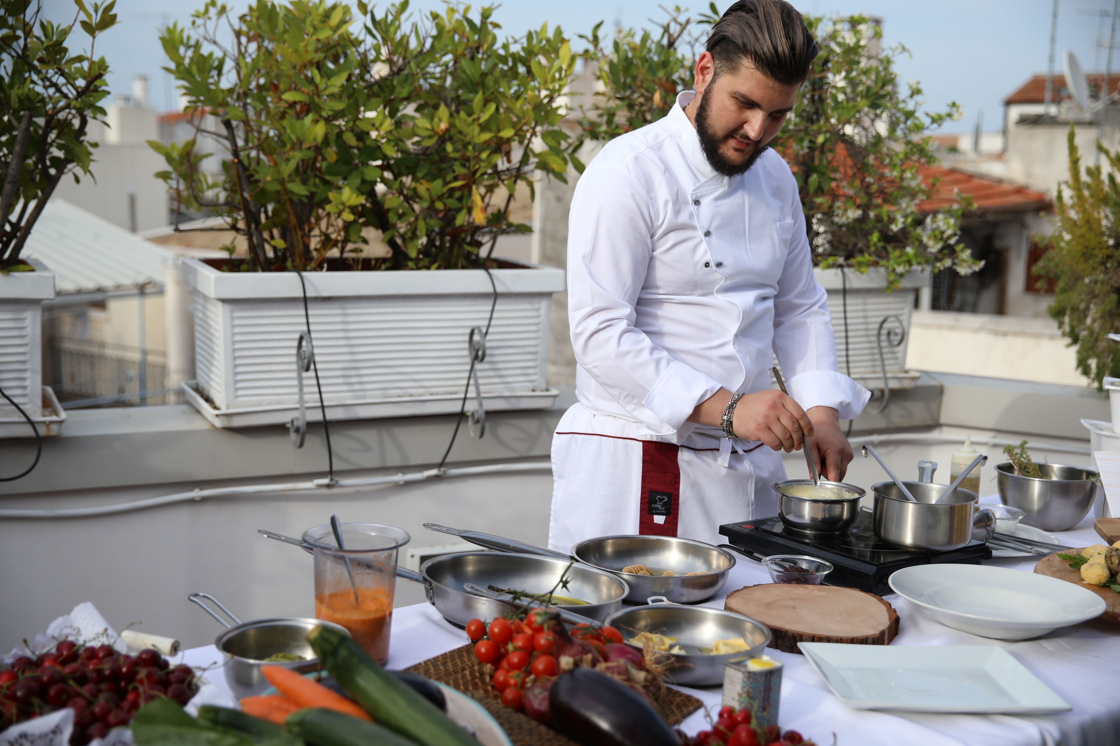 A chef preparing food on a rooftop with a table full of vegetables and cooking utensils.