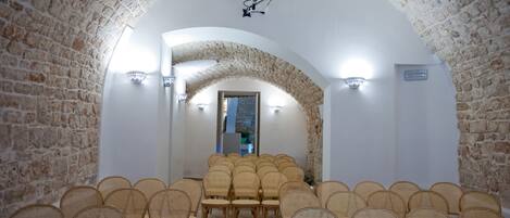 An arched room with stone walls, wicker chairs arranged in rows, and a projector mounted on the ceiling.