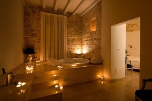 Un cuarto de spa con pared de piedra, una bañera, velas y una cama.