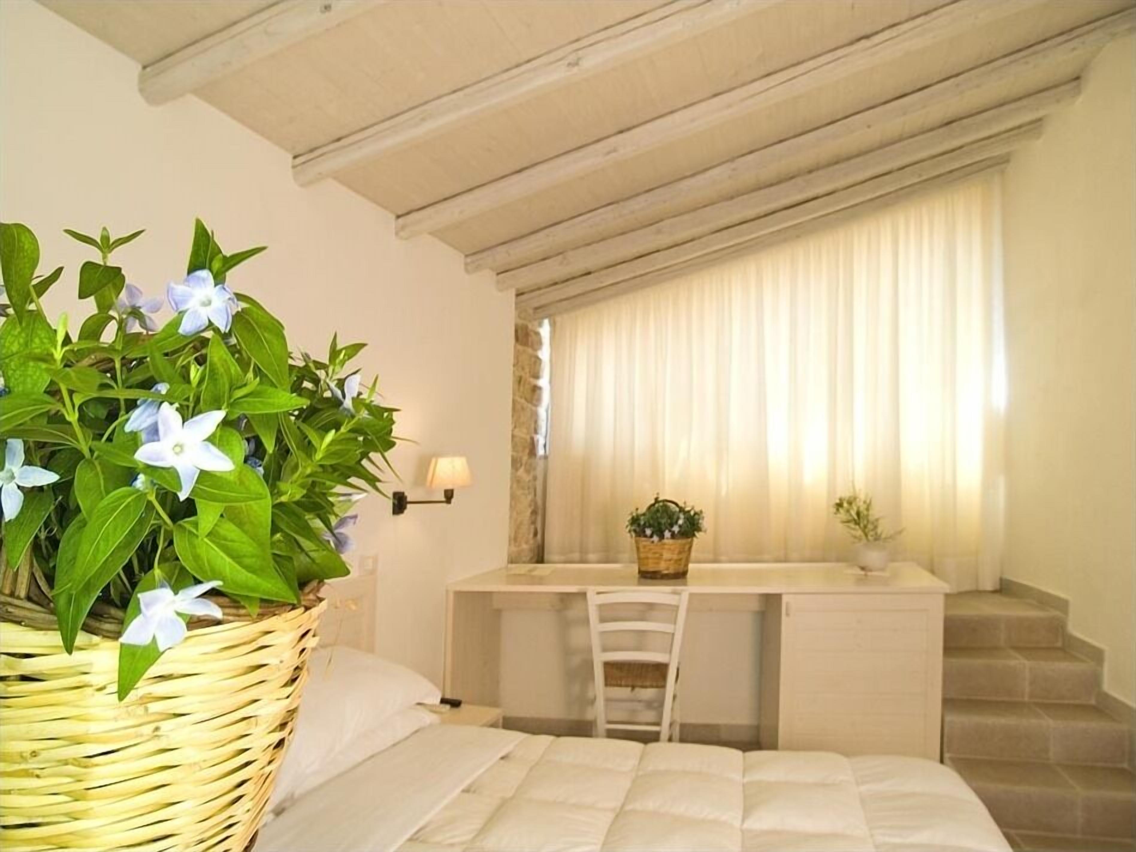 A bedroom with a bed, a desk, and a chair. There is a window with curtains and a plant on the desk.