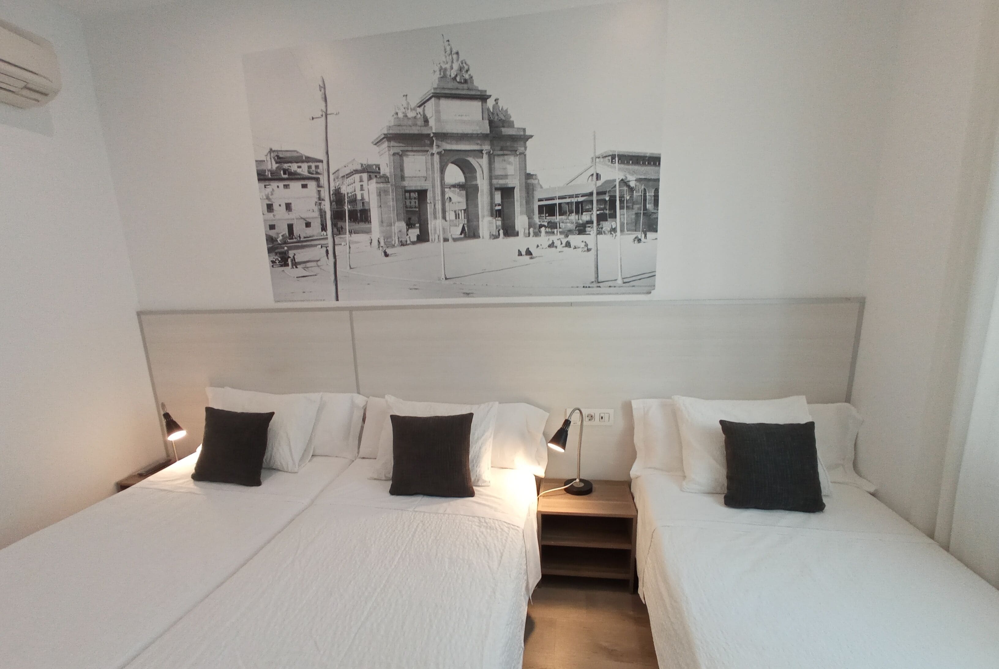 A hotel room with two beds, a nightstand with a lamp, and a wall-mounted picture of an archway.