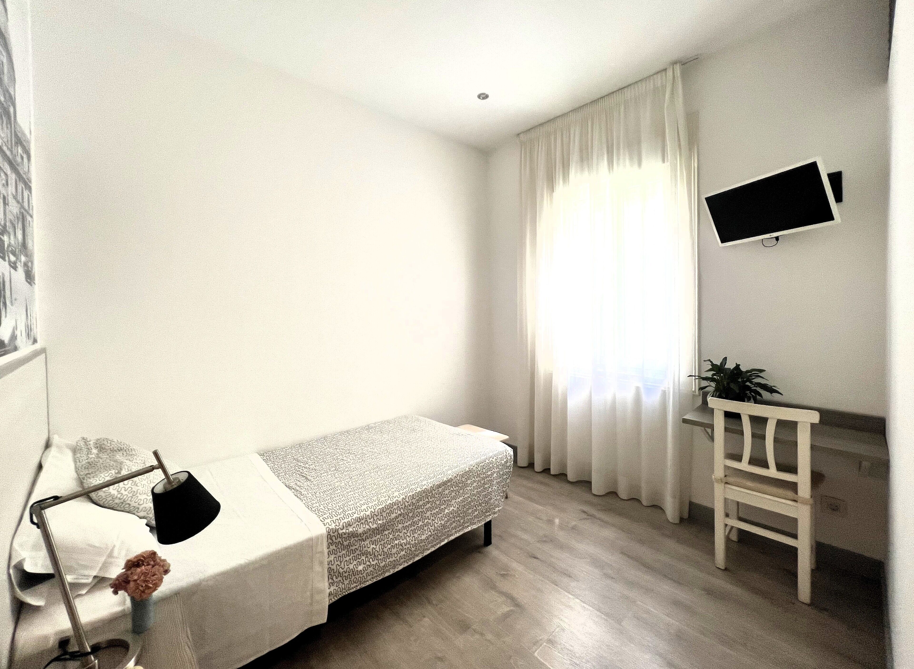 Un dormitorio pequeño y ordenado con una cama individual, un escritorio, una silla y un televisor en la pared.