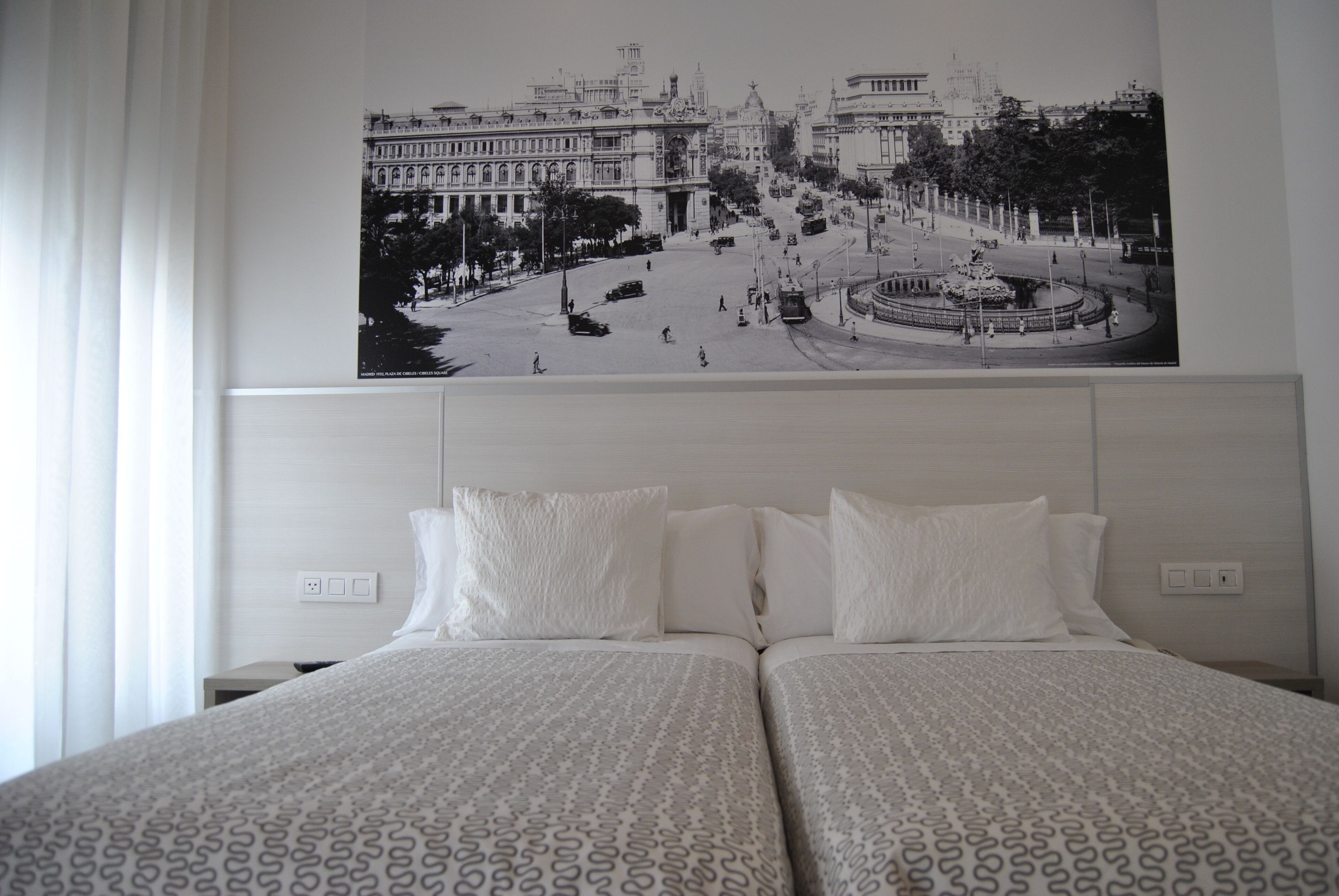 Habitación de hotel con una cama grande, dos almohadas y un cuadro en la pared de un paisaje urbano.