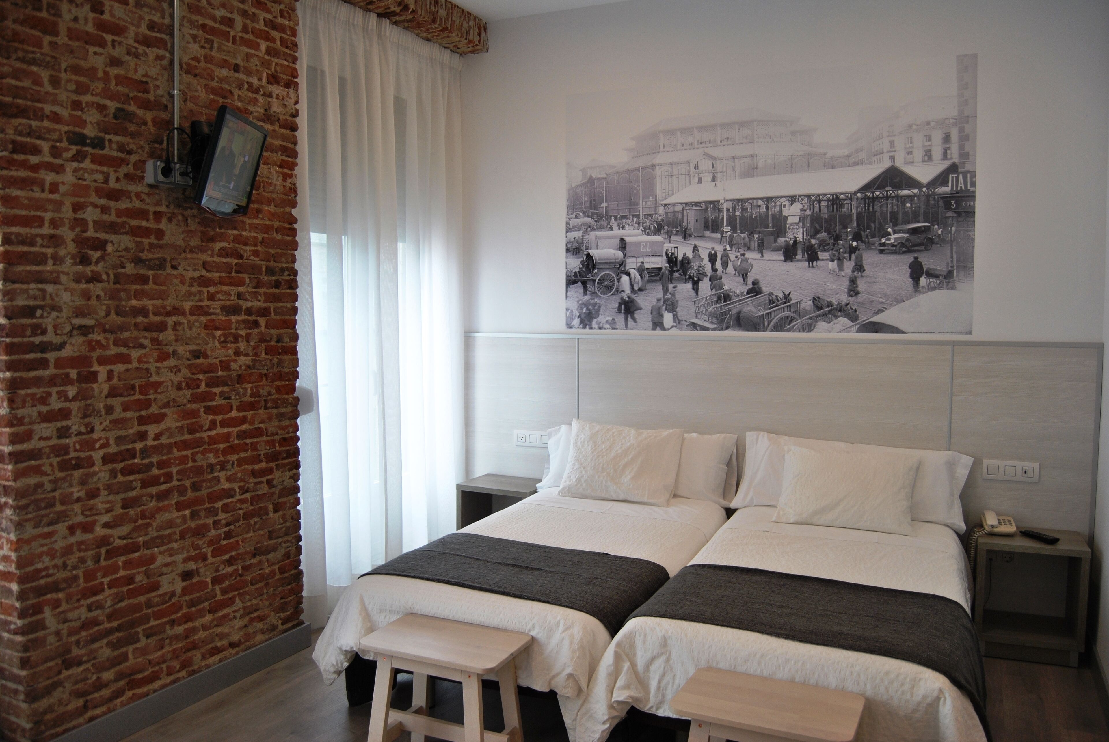 Habitación de hotel con pared de ladrillo, una cama grande con dos almohadas, un taburete de madera y una mesita de noche con un teléfono.